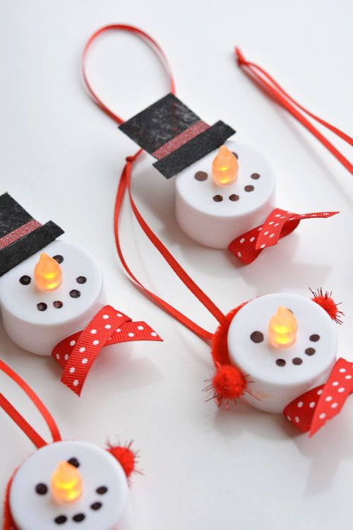 three snowmen made out of toilet rolls with lights on them and red ribbon around the eyes