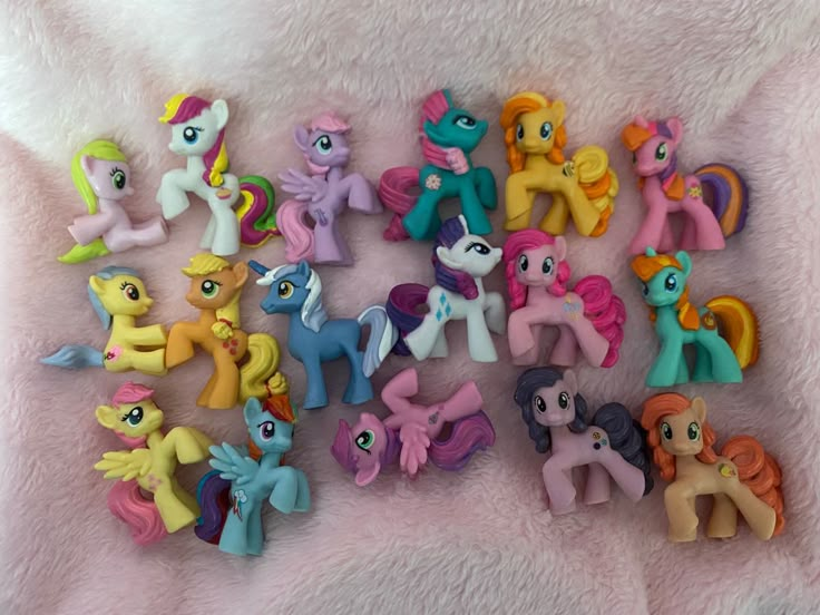 a bunch of little pony figurines sitting on top of a pink blanket