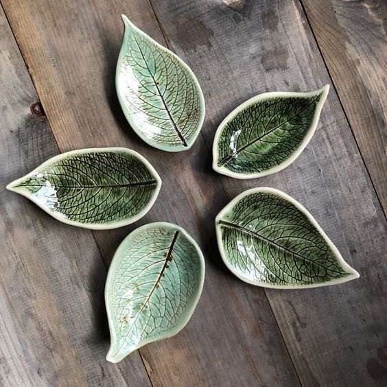 four green leaf shaped dishes sitting on top of a wooden table