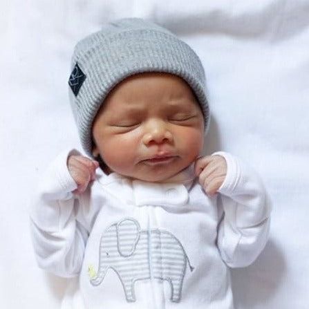 a newborn baby is wearing a hat and sleeps on a white sheet with an elephant design