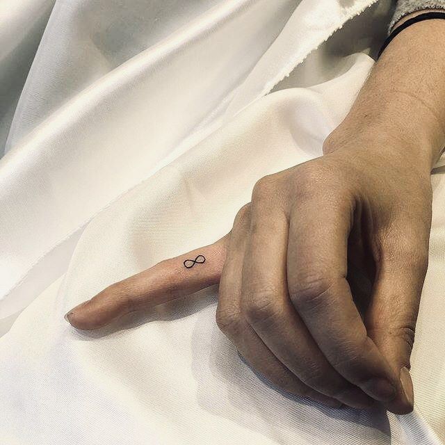 a person's hand with a small tattoo on it, resting on a white sheet