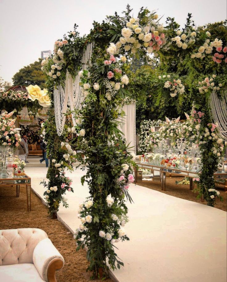 an outdoor wedding setup with white and pink flowers on the arch, greenery and chairs