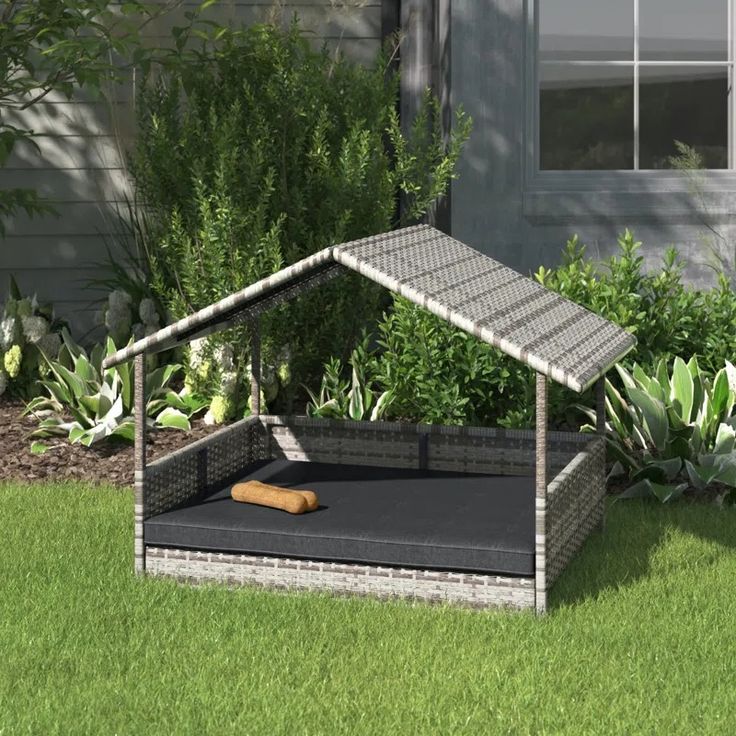 a dog house made out of wicker in front of some plants and grass with a wooden stick sticking out of it