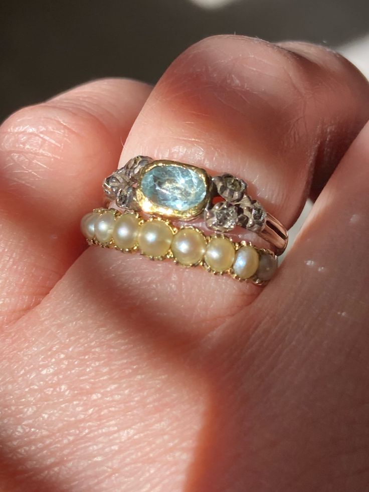 a woman's hand holding a ring with pearls and an aqua topazte