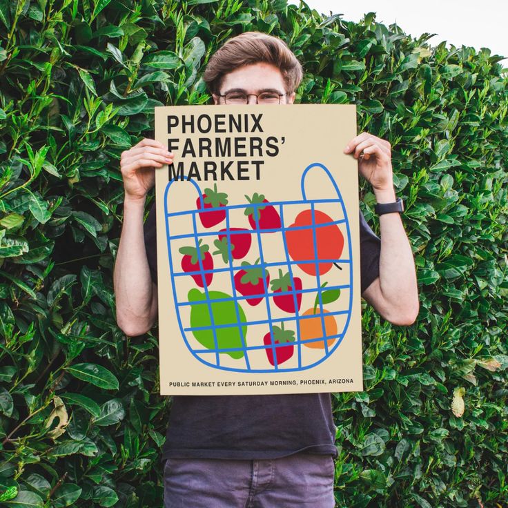 a man holding up a sign that says phoenix farmers'market on it