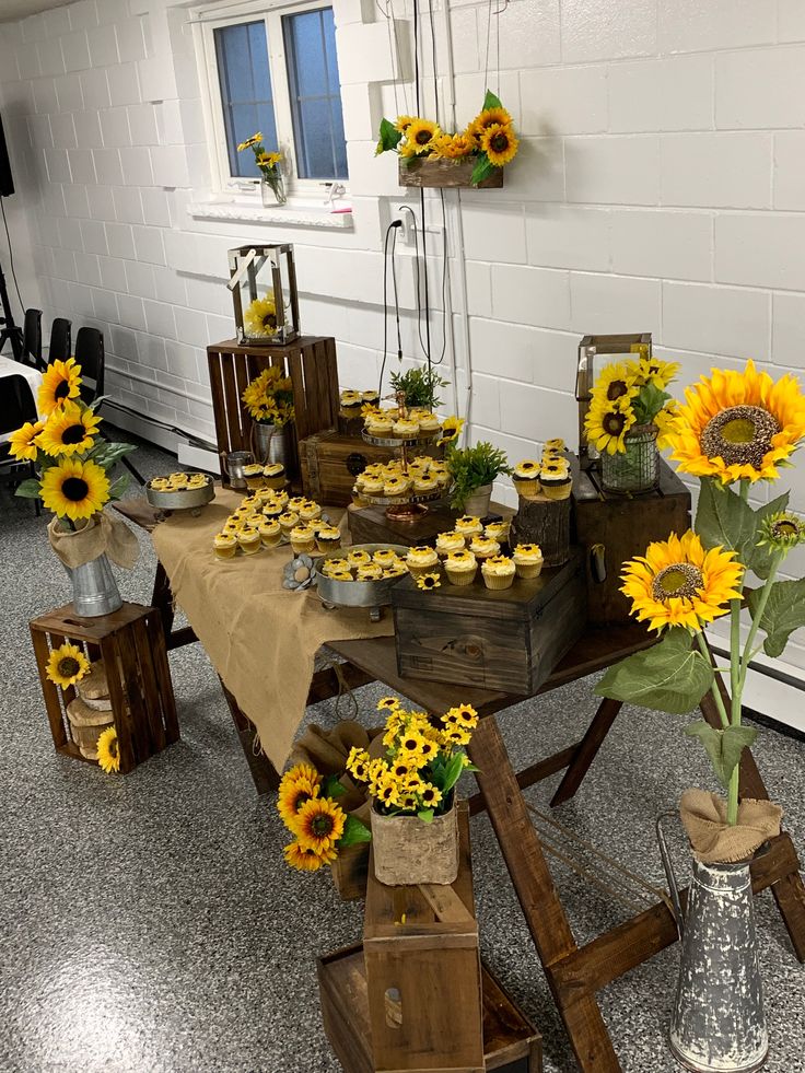 a table topped with lots of cupcakes and sunflowers