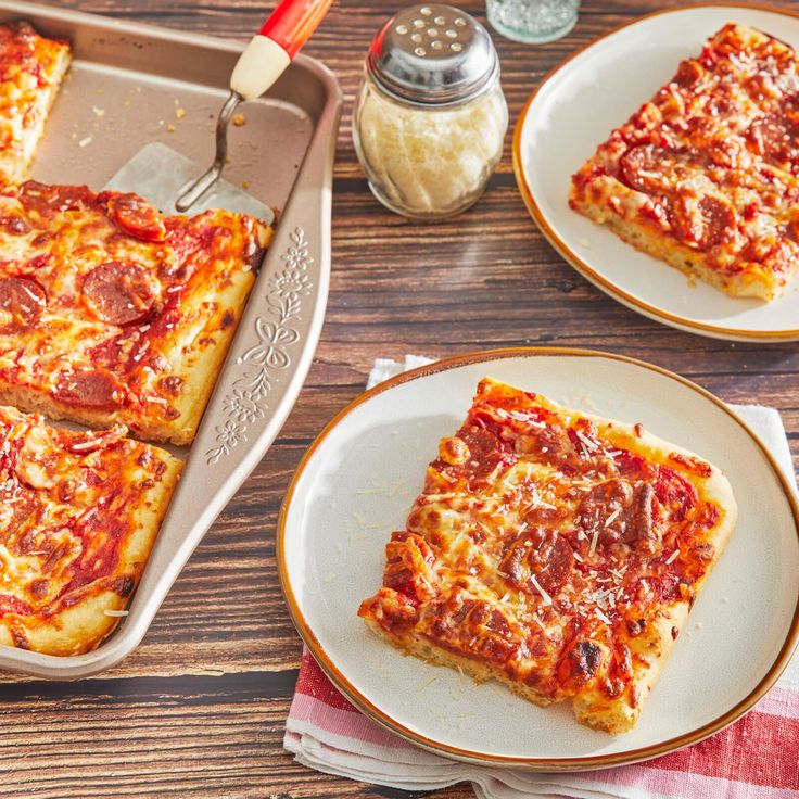 two slices of pizza sitting on top of white plates next to a spatula and fork