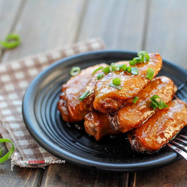 a black plate topped with meat covered in sauce and scallions on top of a wooden table