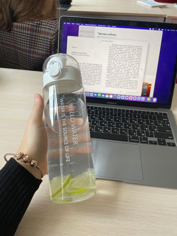 a person holding a water bottle in front of a laptop on a table with a woman's hand