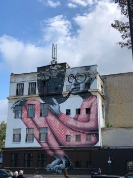 a large mural on the side of a building with people walking by and cars parked in front