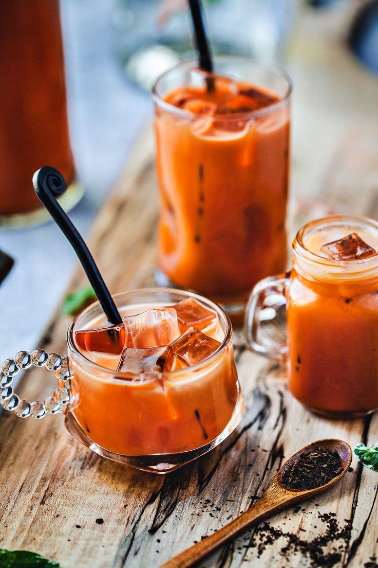 two glasses filled with drinks sitting on top of a wooden table next to spoons