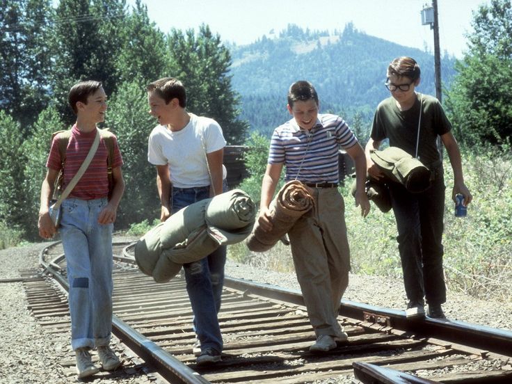 three men are walking on train tracks with bags and backpacks in their hands while another man is carrying something behind them