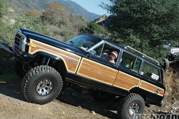 a man driving a brown and black truck on top of a dirt road next to trees