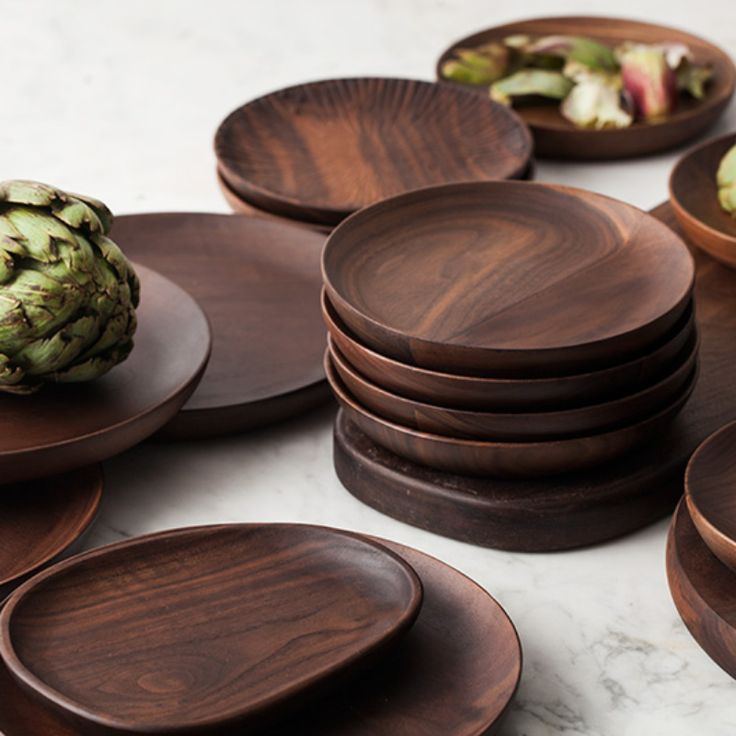 a pile of wooden plates sitting on top of a white marble counter next to an artichoke