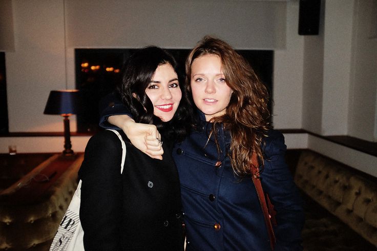 two women standing next to each other in front of a couch and table with lights on it