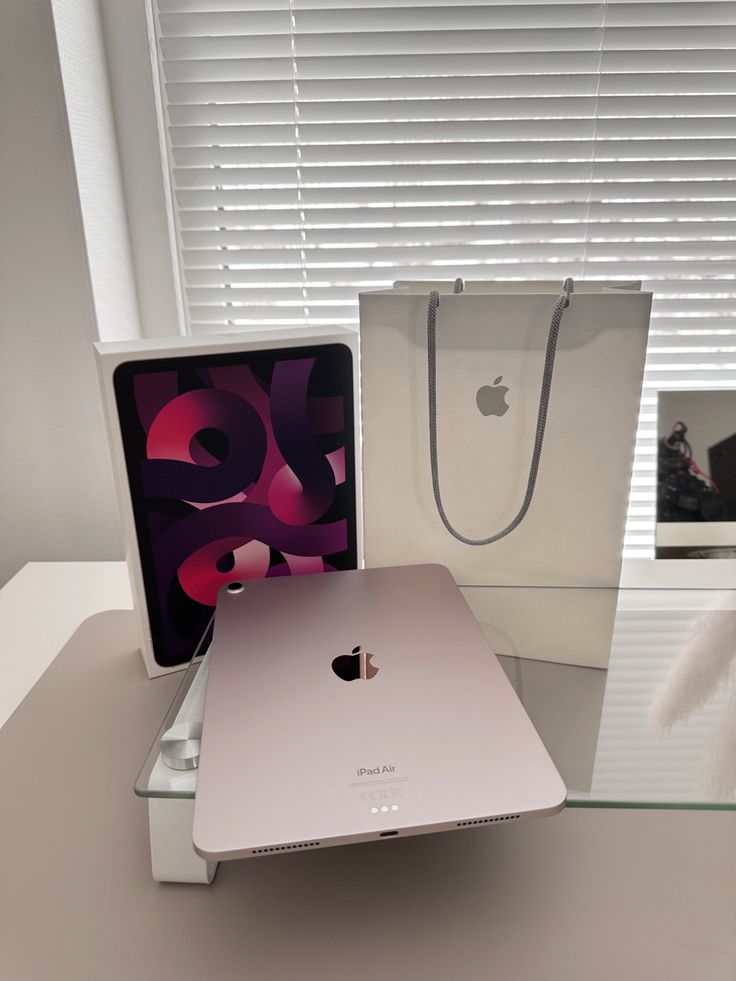 an apple laptop sitting on top of a glass table next to a bag and phone