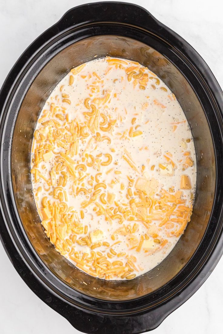 an overhead view of a crock pot filled with cheese and noodles, ready to be cooked