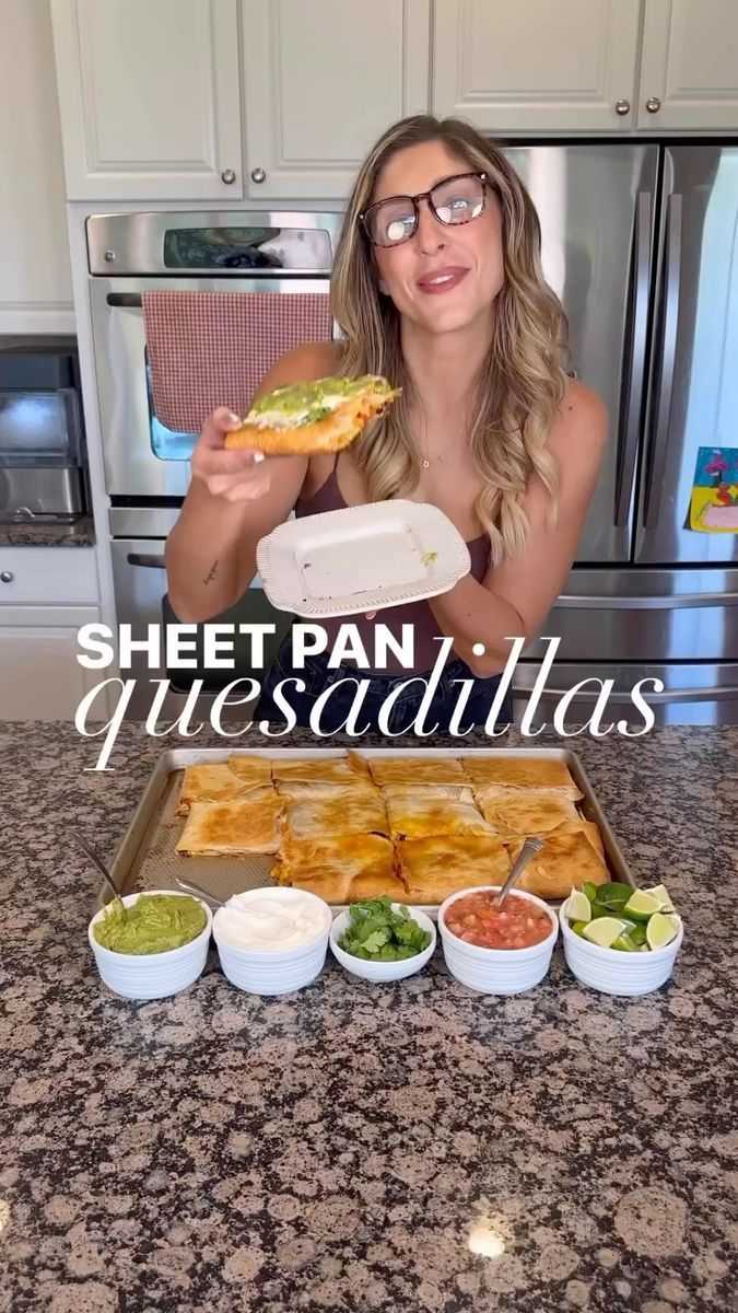 a woman holding a sandwich in front of her face while sitting at a kitchen counter