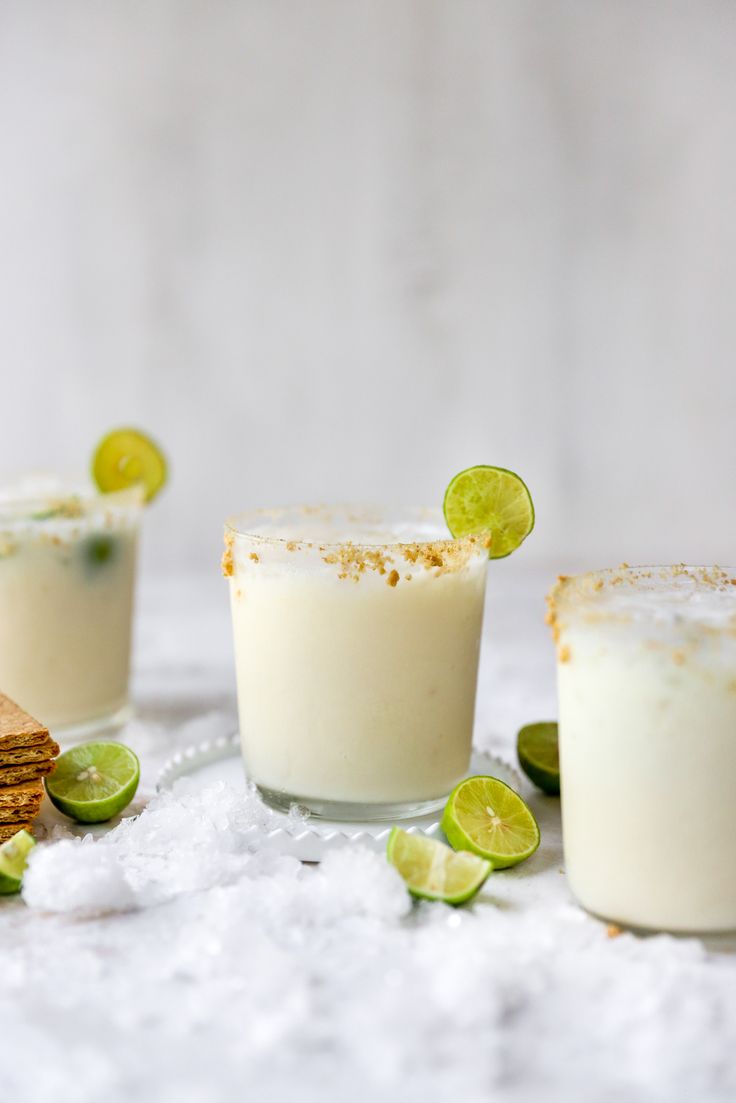 three small glasses filled with different types of drinks and garnished with limes