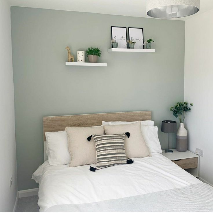 a bed with white sheets and pillows next to two potted plants on the wall