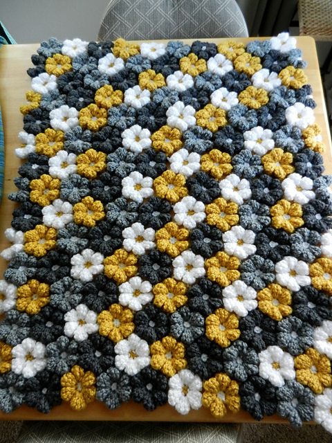 a crocheted blanket with yellow and white flowers on it sitting on top of a wooden table