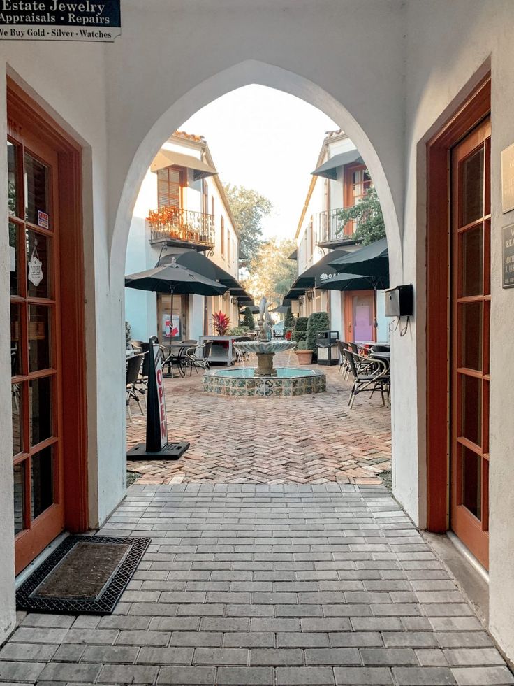 an archway leading into a courtyard with tables and umbrellas