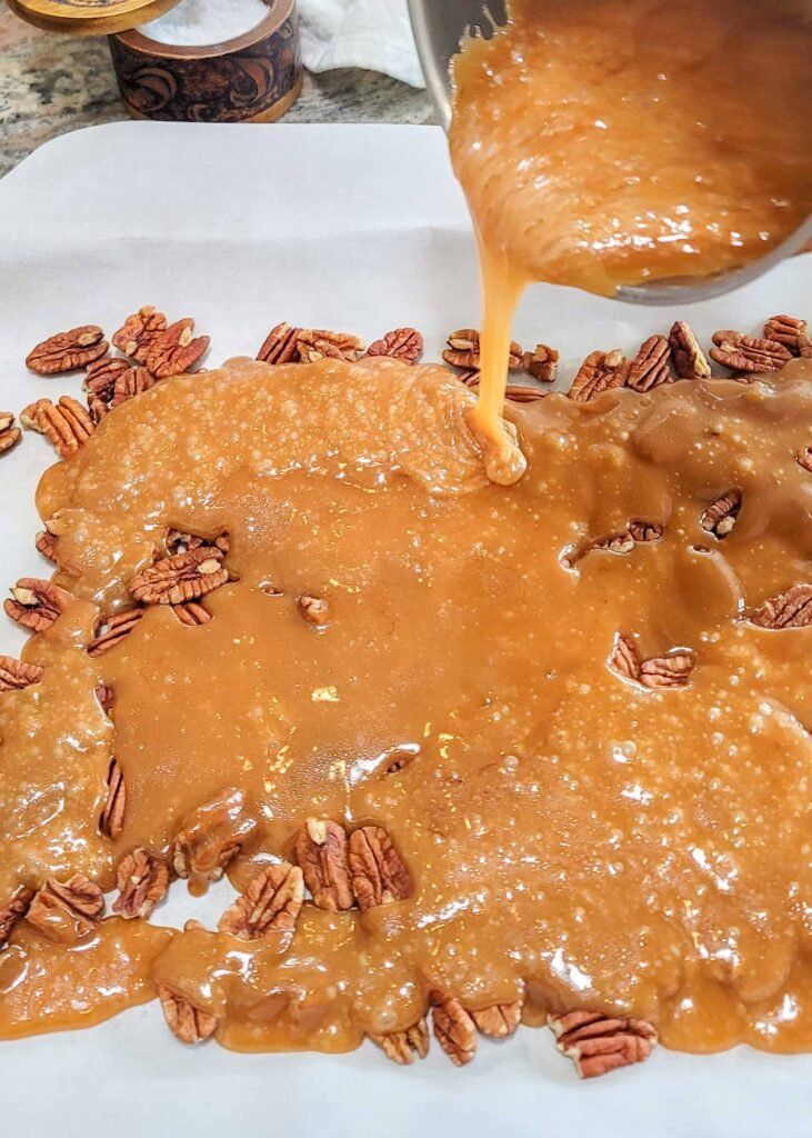 caramel sauce being poured over pecans on white paper