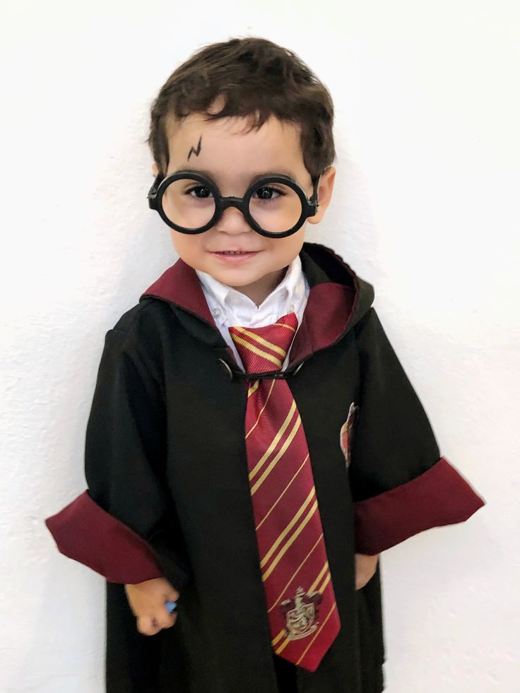 a young boy dressed up as harry potter with glasses and a tie, standing in front of a white wall