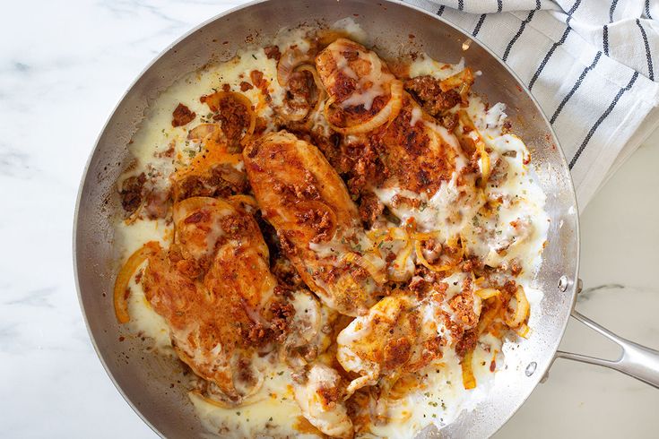 a pan filled with chicken and cheese covered in sauce on top of a marble counter