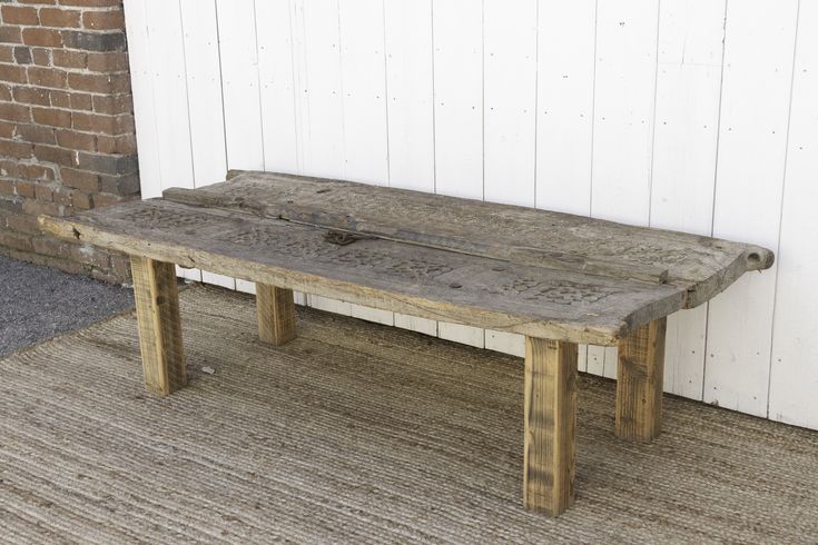 an old wooden table sitting in front of a brick wall with white paint on it