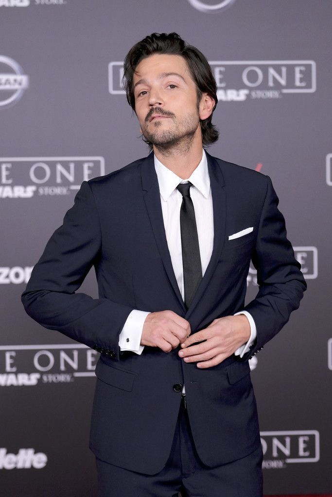 a man in a suit and tie standing on a red carpet with his hands in his pockets