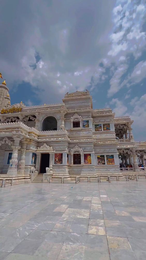 a large white building with statues on the front and side of it, under a cloudy blue sky