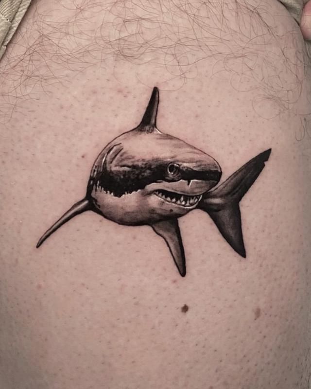 a shark tattoo on the back of a man's thigh, with his mouth open