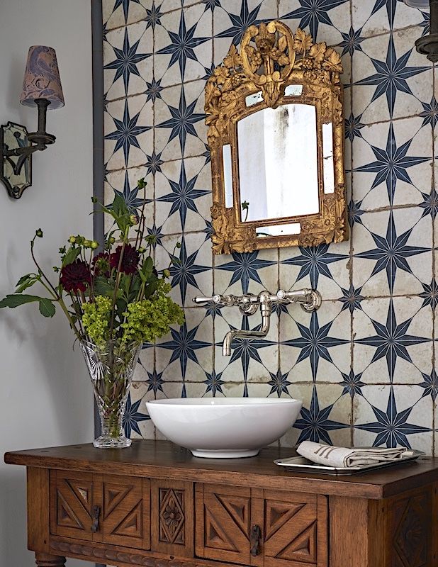 a bathroom sink sitting under a mirror on top of a wooden cabinet next to a vase with flowers