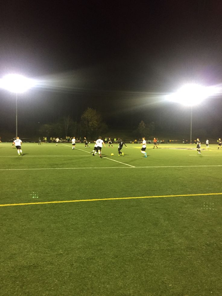 a group of people playing soccer on a field at night with lights in the background