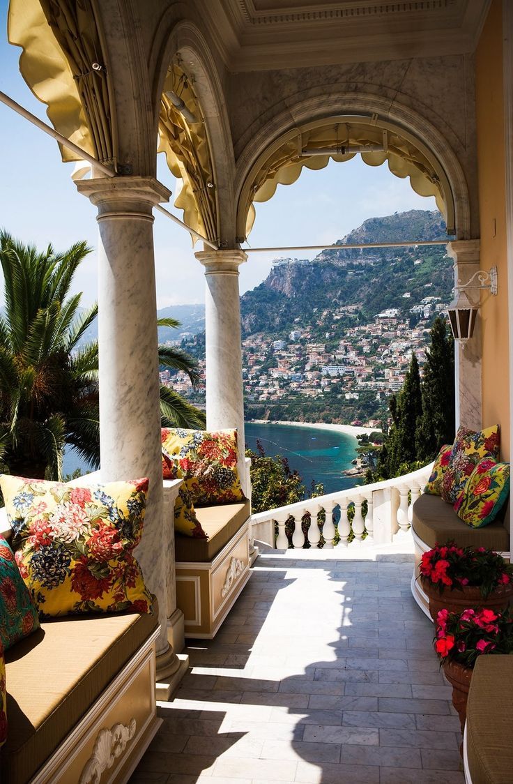 an outdoor covered patio with lots of seating and flowers on the bench, looking out over the water