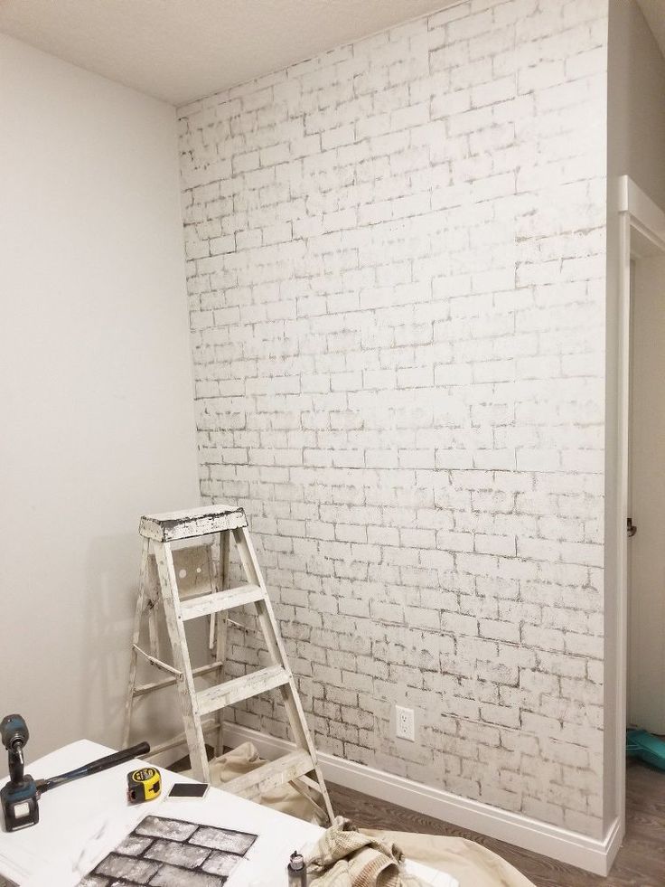 a white brick wall in a room with tools on the floor and a ladder leaning against it