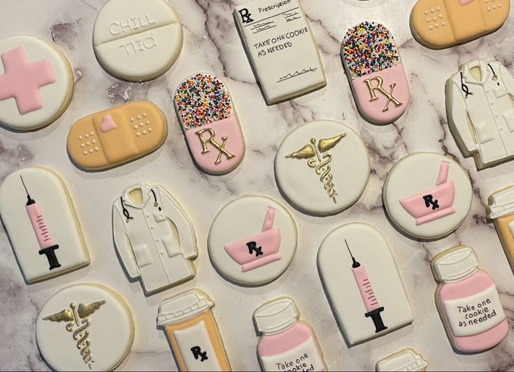 decorated cookies are arranged on a marble surface with pink and white icing in the shape of medical equipment