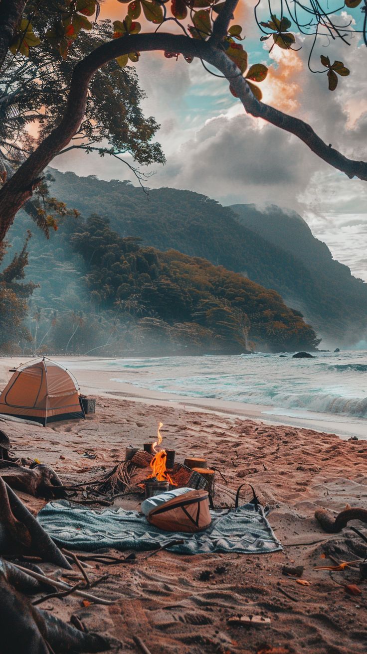 there is a campfire on the beach with a tent in the foreground and mountains in the background