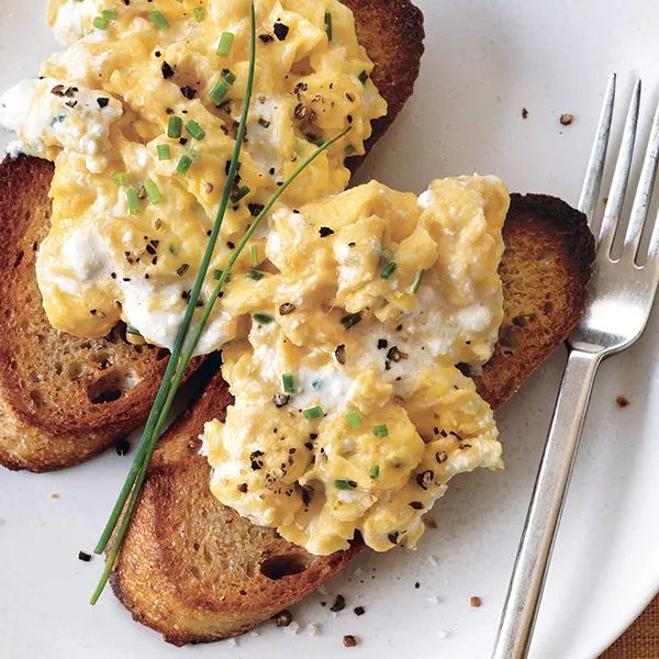 two pieces of toast with eggs and chives on them next to a knife and fork