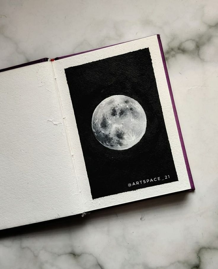 an open book with a drawing of the moon on it's cover, sitting on a marble surface