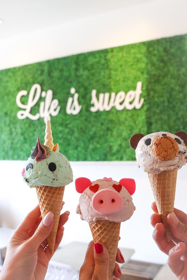 three people holding ice cream cones with animals on them in front of a green wall