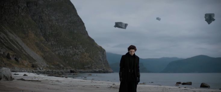 a man standing on top of a sandy beach next to mountains and flying kites