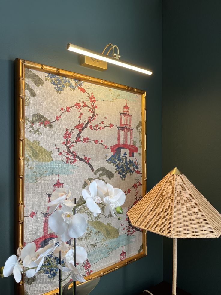 a lamp sitting on top of a wooden table next to a wall hanging with flowers