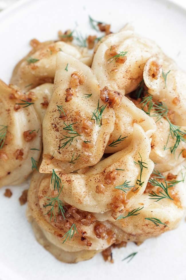 a white plate topped with dumplings covered in sauce and garnished with herbs