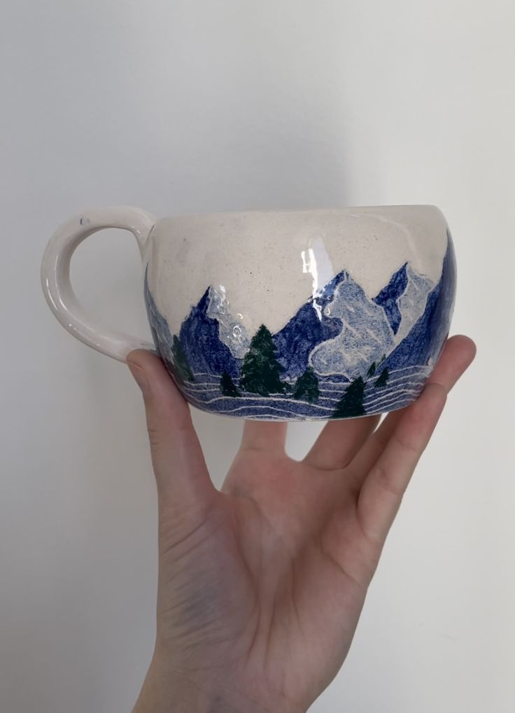 a hand holding a white and blue cup with mountains on it