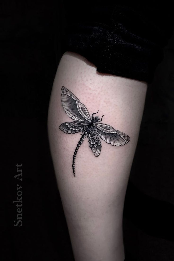 a black and white photo of a dragonfly tattoo on the right thigh, with wings spread out