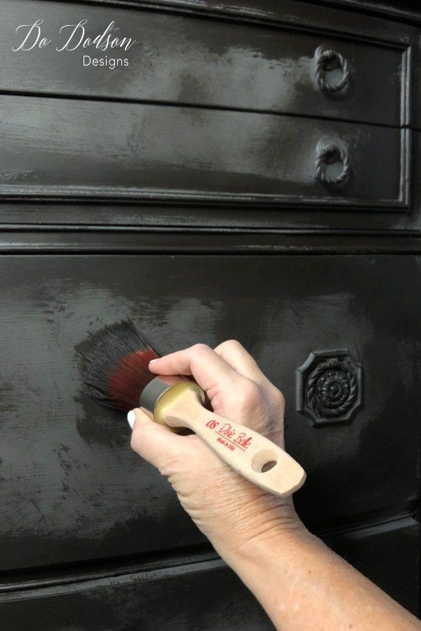 a person using a brush to clean an old dresser drawer with black paint on it