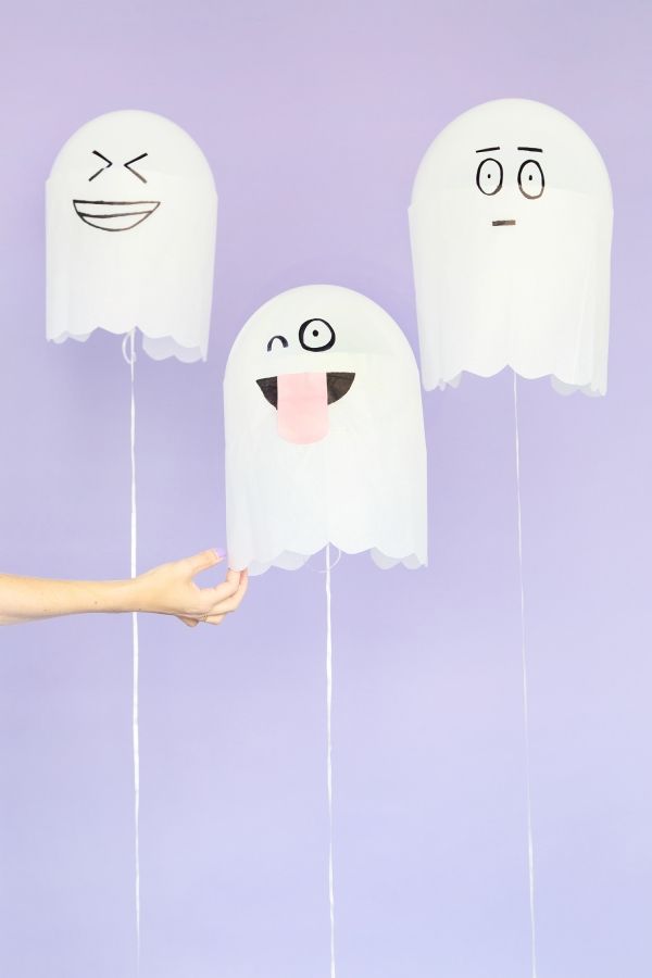 three paper ghost heads are being held up by two hands