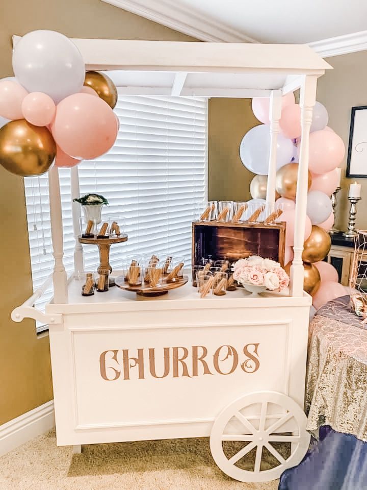 a white cart with balloons and other items on it in front of a table that says churros